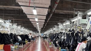 Busy clothing manufacturing factory with workers and hanging black garments on production lines