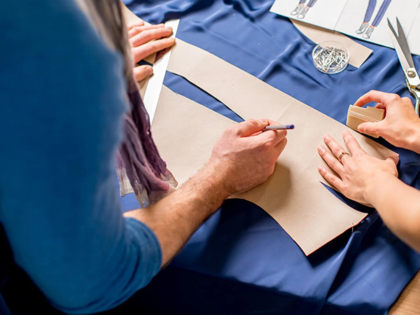 Designers drafting garment patterns on blue fabric with leggings sketches, scissors, and pins on the worktable.