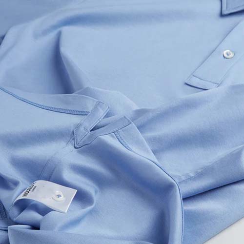 Close-up of a light blue polo shirt showing the collar, sleeve, and care tag with QR code, neatly folded.