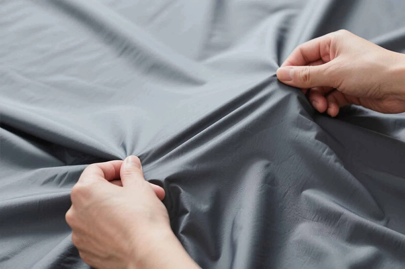 Hands stretching smooth lightweight gray fabric showing flexibility and soft texture