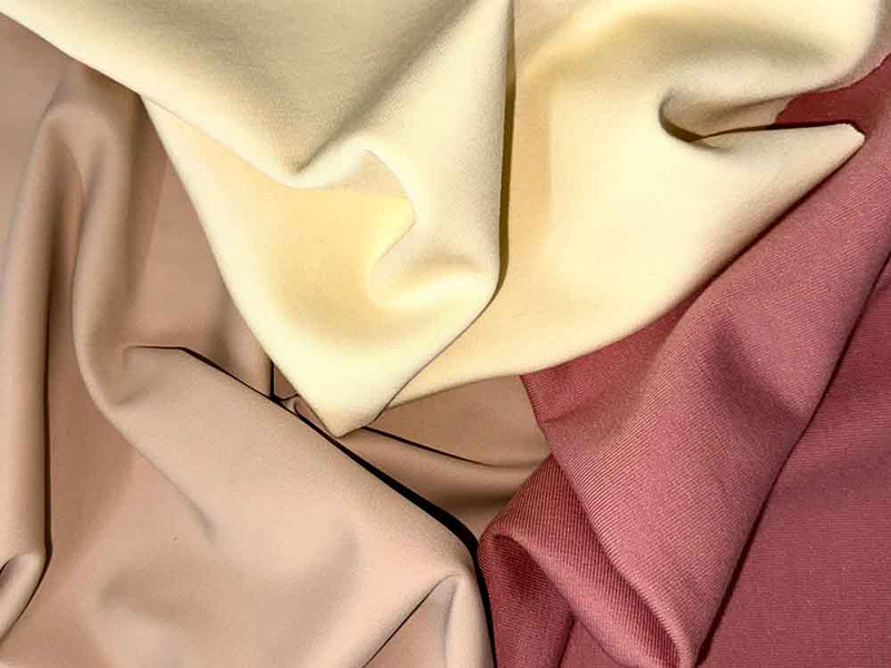 Four pieces of fabric in soft, muted shades of cream, beige, light brown, and dusty rose, arranged overlapping with gentle folds.