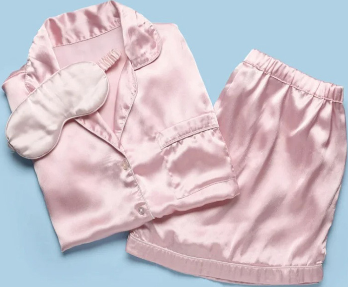 A folded pink satin pajama set laid out on a light blue background.