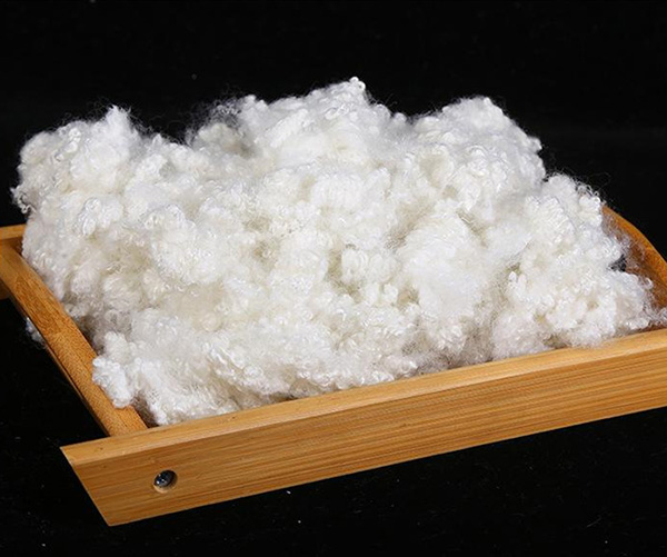 White polyester fiber filling piled in a shallow wooden tray on black background.