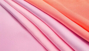 Various folded pink and coral ribbed fabrics laid out together for clothing.