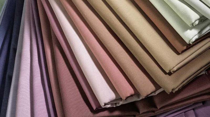Close-up of neatly folded fabrics in soft neutral shades including purple, pink, beige, and brown, layered in a fan-like arrangement.