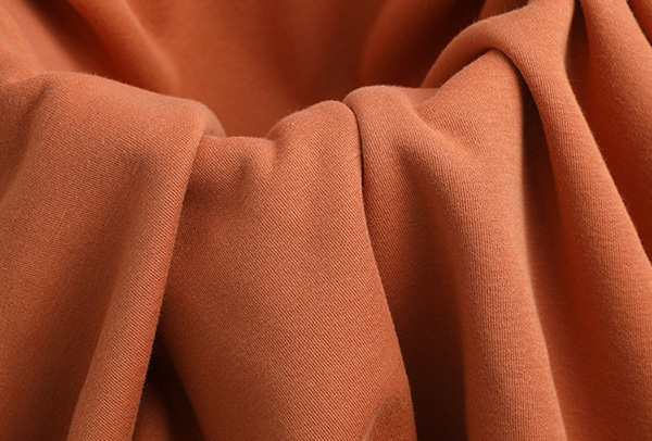 Close-up of rust orange knit French terry fabric draped in soft folds, showing smooth texture.