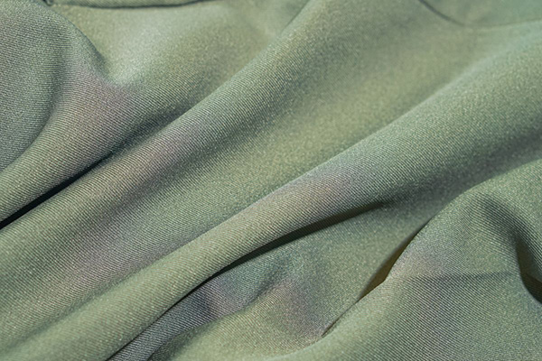 Close-up of sage green knit fabric draped in soft folds with smooth texture.