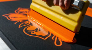 Squeegee spreading bright orange ink during screen printing on dark fabric