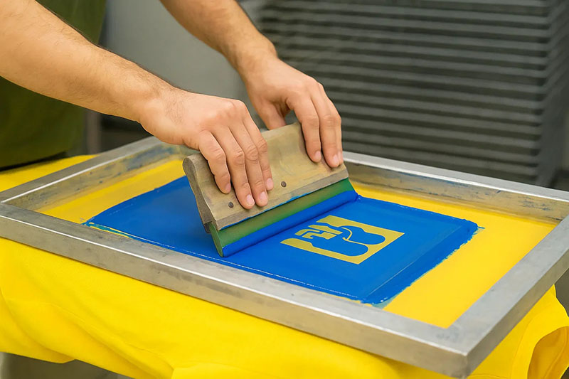 Hands using squeegee to apply ink during screen printing on fabric