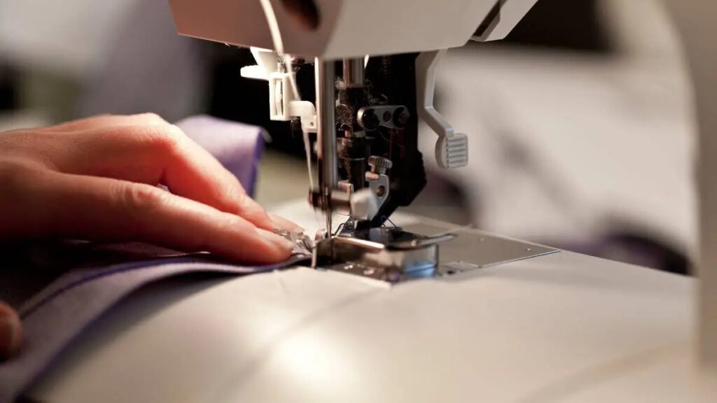 Close-up of hands guiding fabric through a sewing machine during garment stitching.