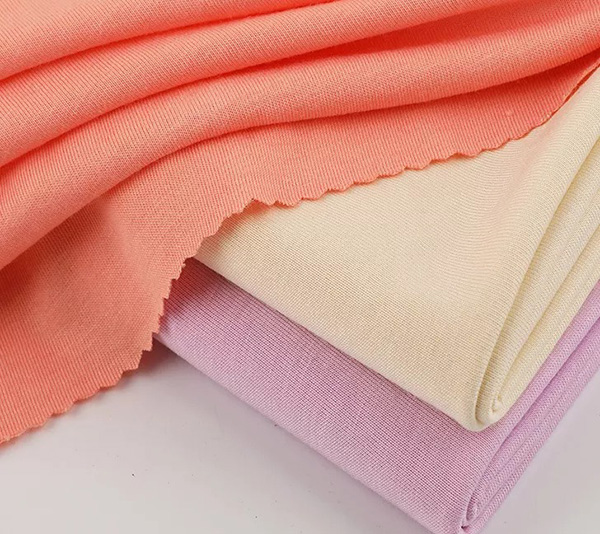 t: Three pieces of folded fabric in pastel shades tacked on a white surface with the top coral fabric slightly draped.