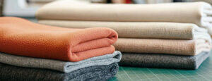 Folded sweatshirt fabrics in various neutral and warm colors on a table.