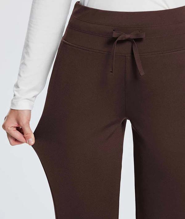 Close-up of a person wearing dark brown stretchable pants with a drawstring waistband, pulling fabric to show elasticity.