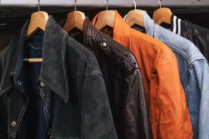 Assorted leather and denim jackets hanging on wooden hangers in a fashion display