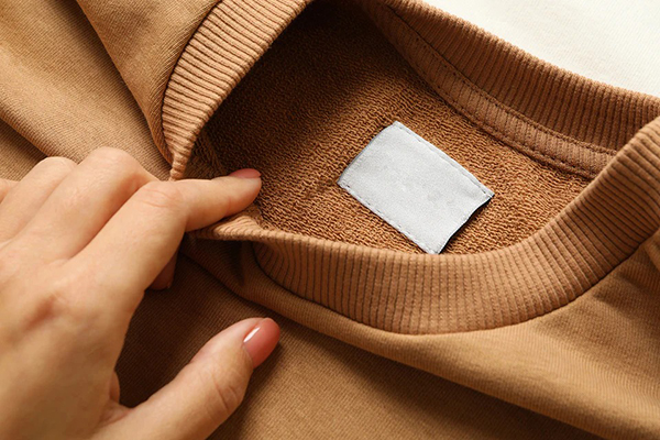 Hand lifting tan sweatshirt collar to show soft loopback terry interior and label.