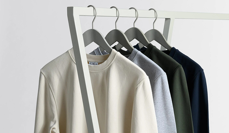 Crewneck sweatshirts hanging on a rack in cream, gray, olive, and navy colors.