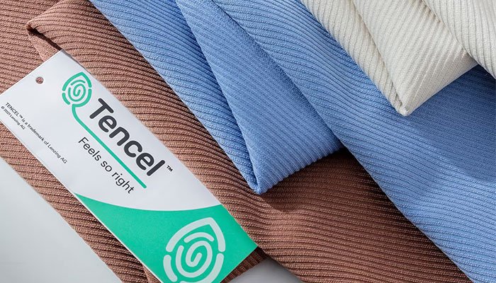 Folded Tencel fabric swatches in brown, blue, and beige with a Tencel label, showing texture and color variety.