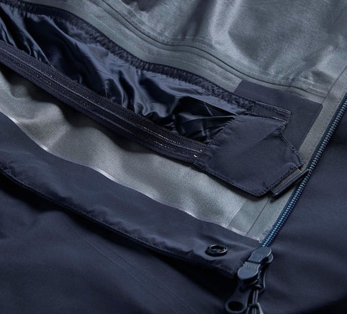 Close-up view of a navy waterproof jacket showing the sealed zipper, storm flap, and interior lining.