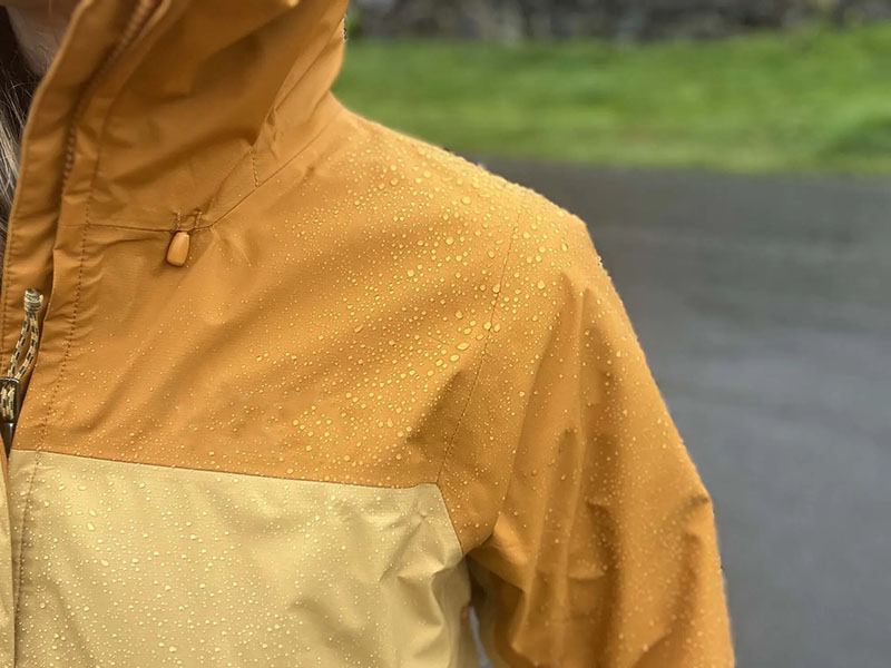 Close-up of a yellow and beige waterproof jacket with water droplets on the fabric.