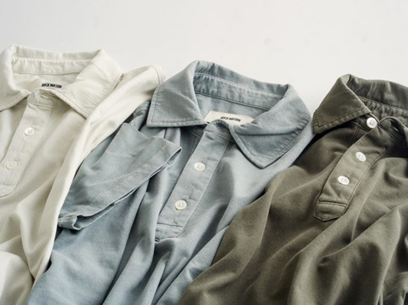 Three soft polo shirts laid out in cream, light blue, and olive green tones.