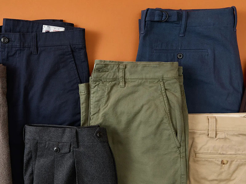 Folded men’s trousers in navy, olive, charcoal, and khaki arranged in a product display.