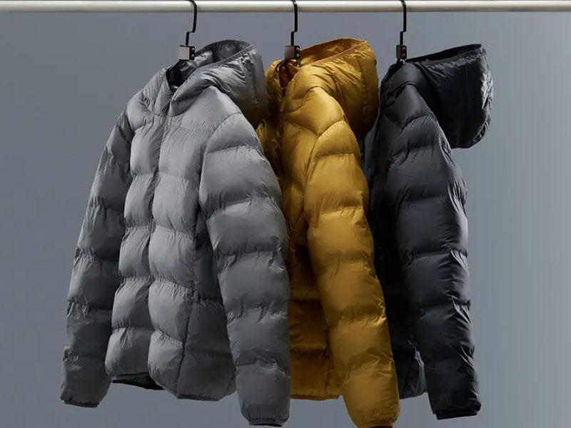 Three hooded puffer jackets in gray, yellow, and black hanging on a clothing rack.