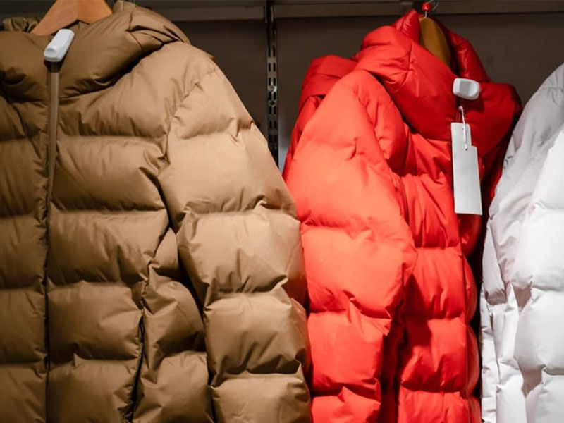 Brown, red, and white puffer jackets hanging on hangers in a clothing store, showcasing winter outerwear.