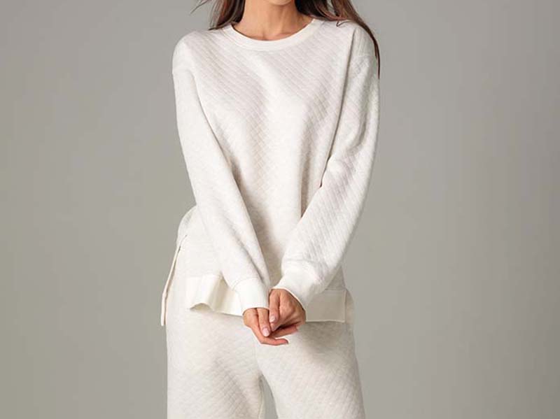 Woman wearing a soft, white quilted long-sleeve top and matching pants, standing with hands clasped.