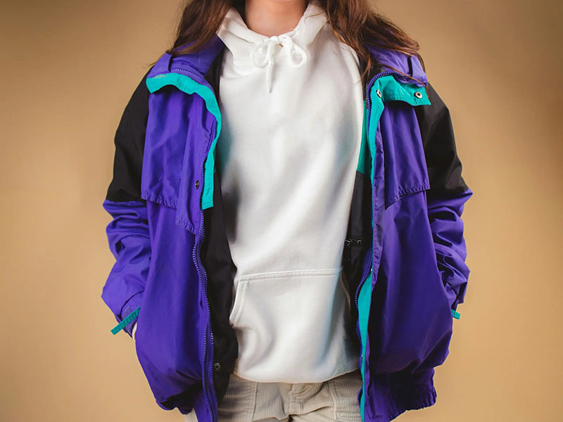 Woman wearing colorful retro windbreaker jacket layered over a white hoodie outfit