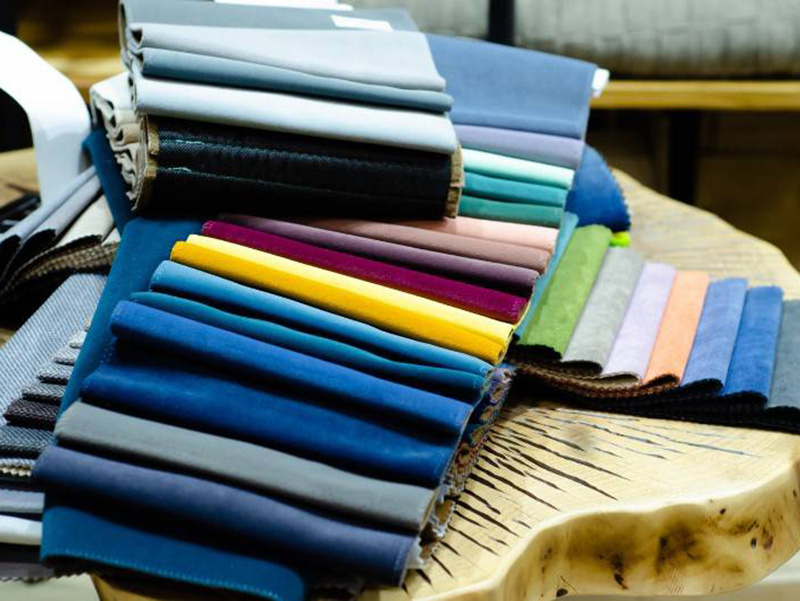 Folded fabric samples in various colors arranged on a wooden table, showing texture and shades