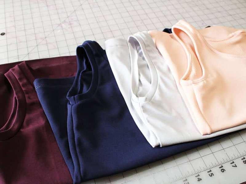 Folded crewneck T-shirts in burgundy, navy, white, and peach colors displayed on cutting table for apparel manufacturing and fashion retail presentation