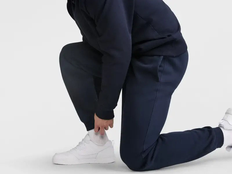 Person kneeling while wearing navy blue jogger pants and white sneakers, showing tapered fit and elastic ankle cuffs