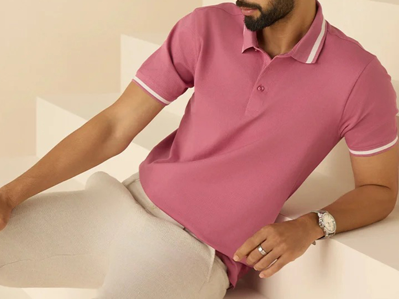 Man wearing a pink polo shirt with white trim on collar and sleeves, styled with light beige pants.
