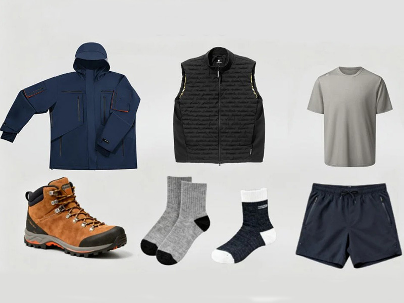 Flat lay of outdoor outfit including navy jacket, black puffer vest, gray t-shirt, brown hiking boots, gray socks, and navy shorts.