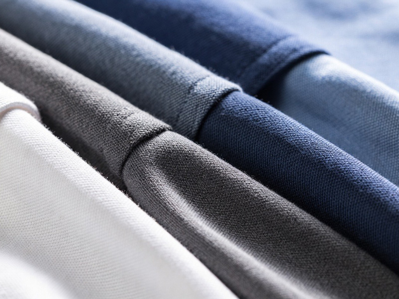 Close-up of folded polo shirts in white, gray, navy, and light blue tones.