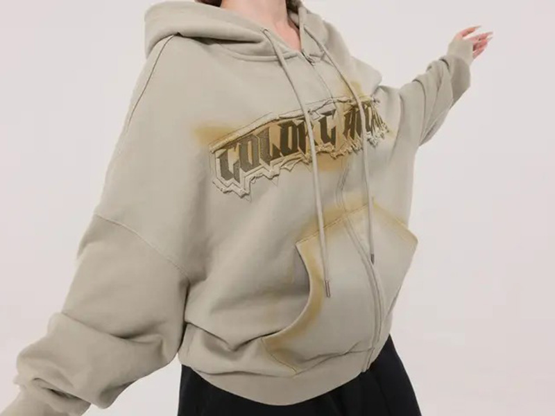 Woman wearing oversized beige graphic hoodie with front pocket and drawstrings.