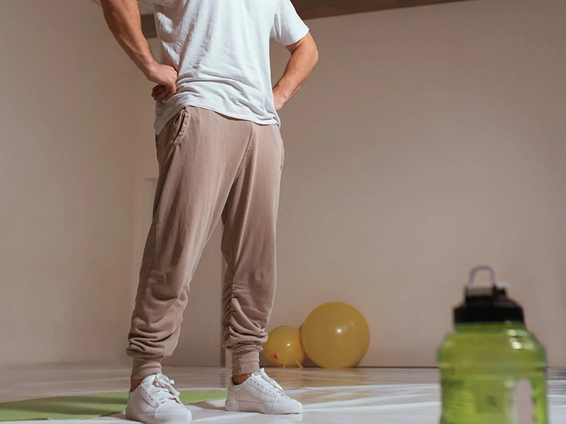 Man wearing beige jogger sweatpants and white T-shirt in a relaxed indoor setting.