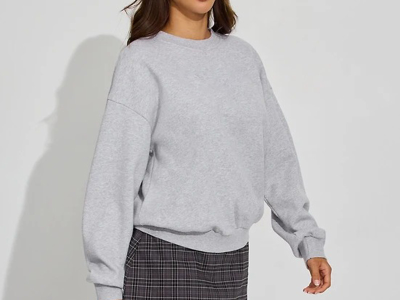 Woman wearing oversized light gray crewneck sweatshirt with dropped shoulders and relaxed fit.