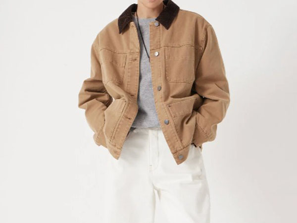 Person wearing a casual brown button-up jacket with black collar over a gray shirt, paired with white pants.