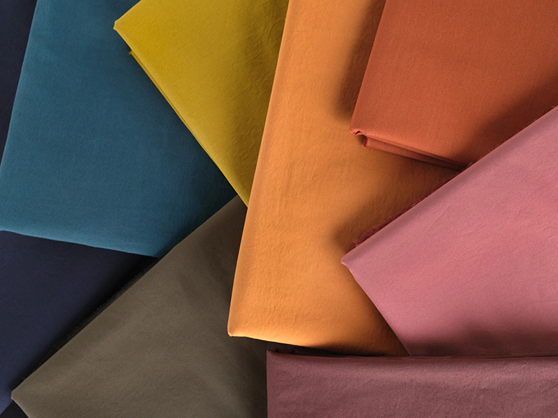 Seven neatly folded fabric swatches in a variety of colors — navy blue, teal, olive green, mustard yellow, orange, rust, and pink