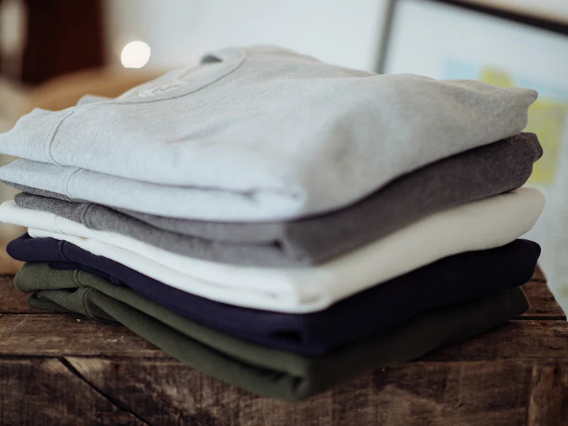 Stack of folded sweatshirts in neutral colors on a rustic wooden table.