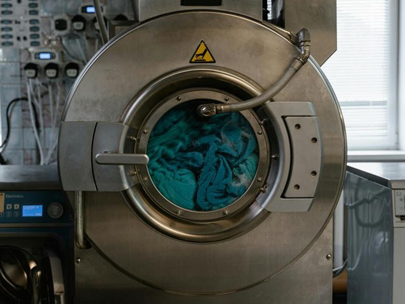 Industrial washing machine cleaning blue textile garments in commercial laundry facility