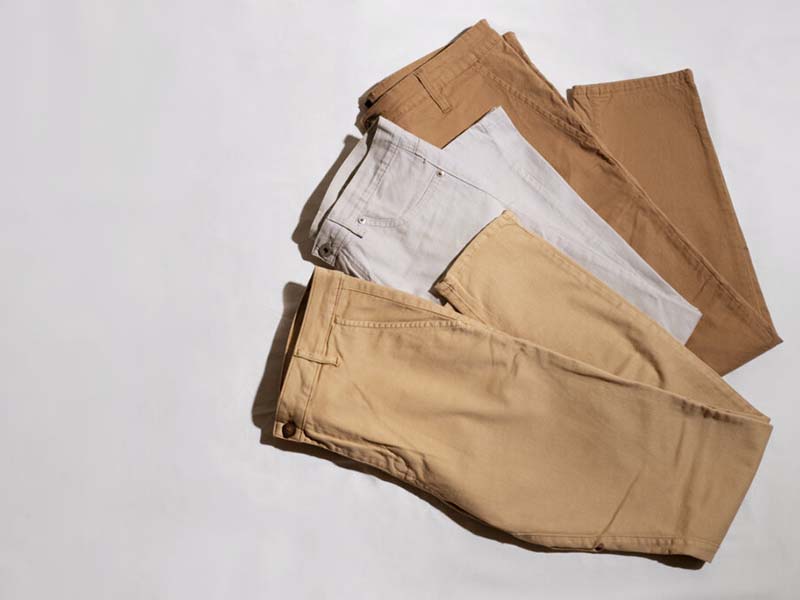 Three pairs of pants in beige, light gray, and brown neatly folded and laid out on a white surface.
