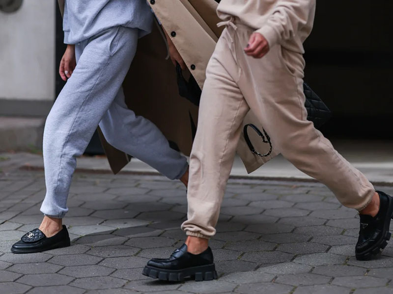 Two people walking outdoors wearing gray and beige cuffed jogger pants paired with black loafers, showcasing comfortable streetwear style