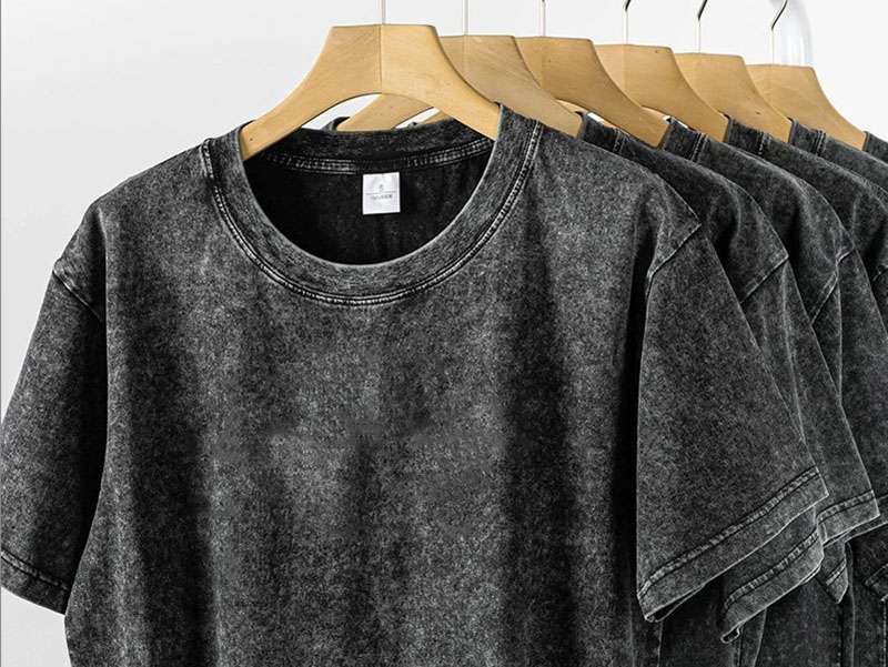 Washed charcoal gray T-shirts hanging on wooden hangers in a row.