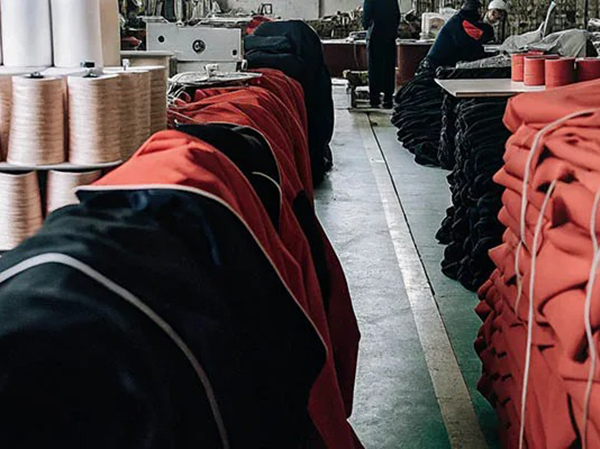 Garment factory aisle with stacked red and black clothing pieces and thread spools.