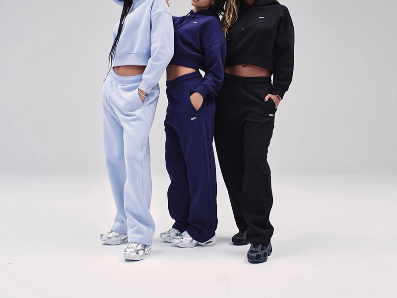 Three women standing side by side wearing matching cropped hoodies and wide-leg sweatpants in different colors
