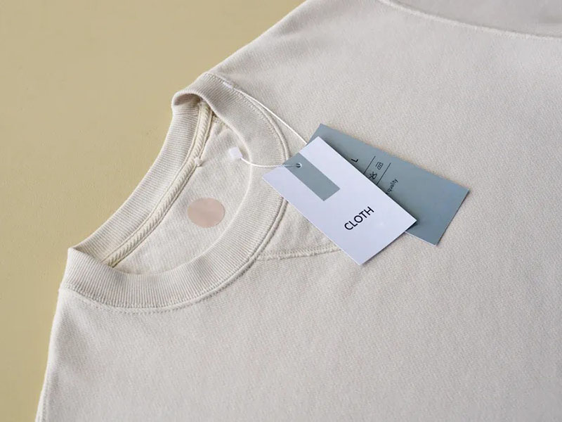 Cream crewneck sweatshirt with clothing tags displayed in clean minimalist fashion product presentation style