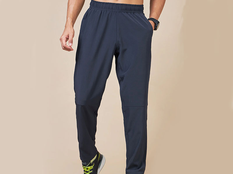 Close-up of a man wearing navy jogger pants with elastic waistband, side pockets, and black running shoes with neon laces.