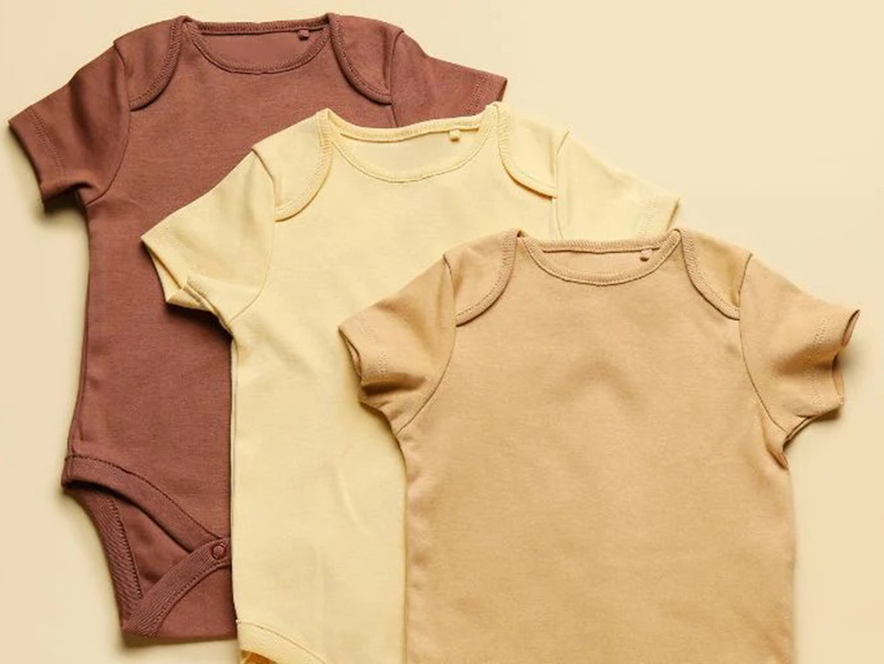 Three baby onesies laid flat in a row, in earthy tones